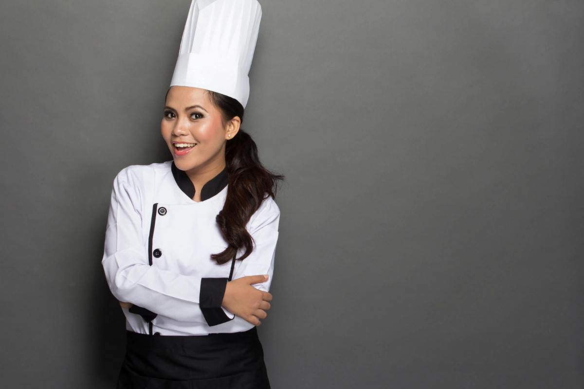 Cocinera profesional con gorro blanco, sonriendo y preparada para cocinar croquetas.