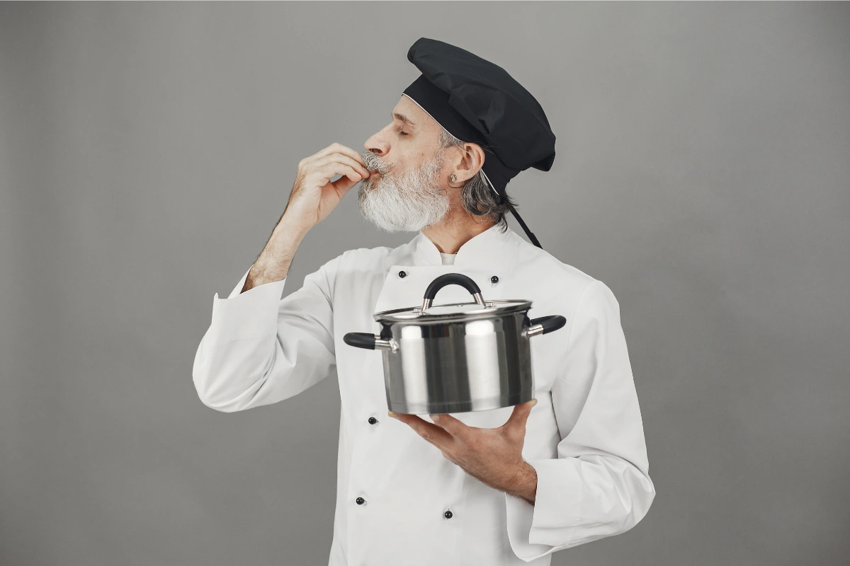 Cocinero profesional con gorro negro y cazuela, evocando la preparación de croquetas.