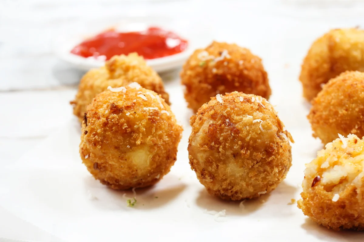 Croquetas redondas caseras con un rebozado crujiente y dorado, acompañadas de salsa.