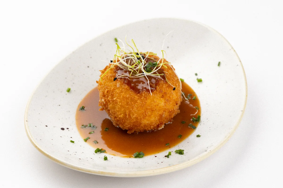 Croquetón Sorpresa, una croqueta de osobuco con base de patata cremosa, rebozada y acompañada de una salsa misteriosa. Participante en Santiago(é)Tapas 2025.
