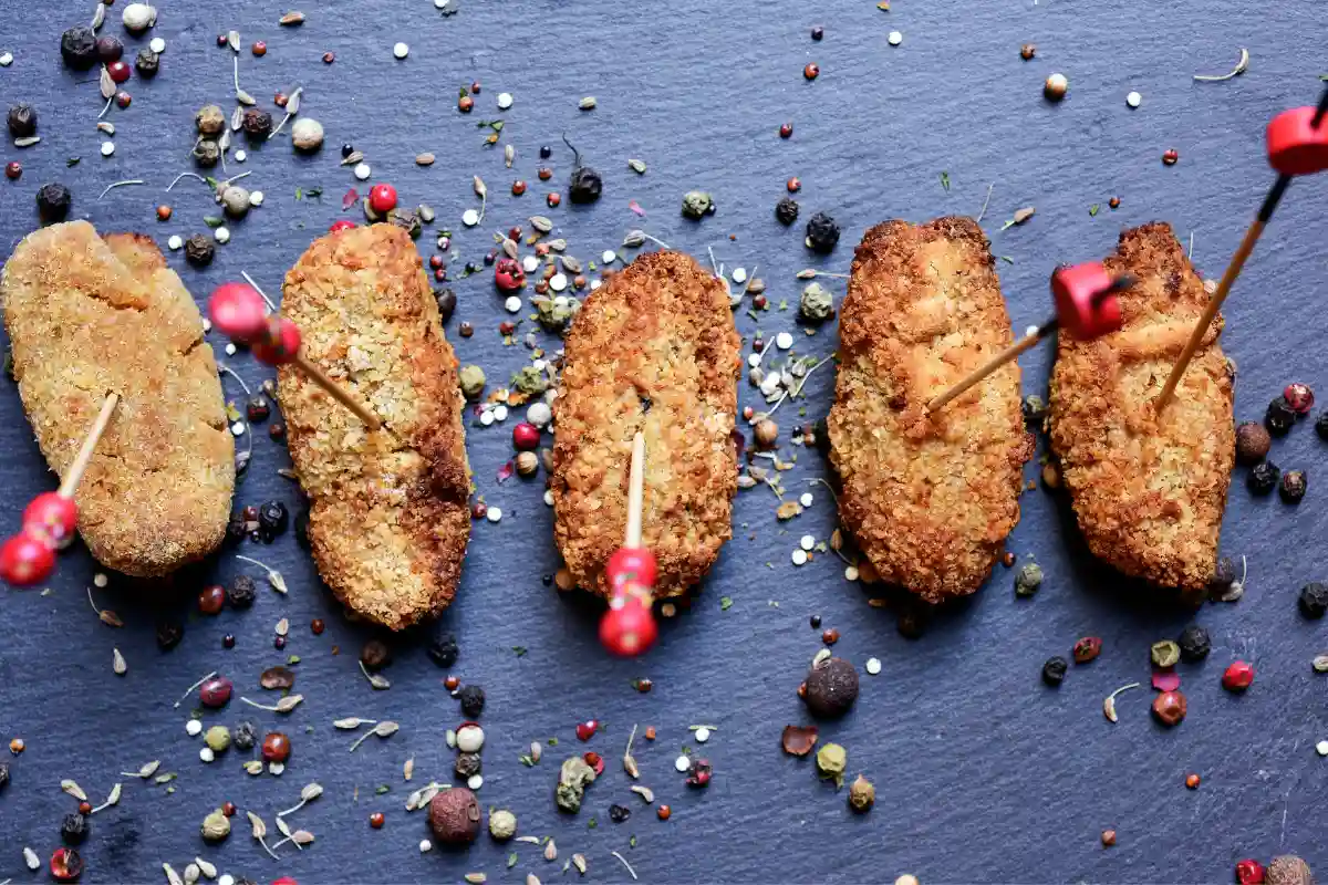Croquetas crujientes con rebozado variado, servidas sobre una pizarra con especias.