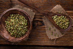 Cuenco con granos de pimienta verde y una cuchara de madera, base para preparar salsa de pimienta verde para croquetas.